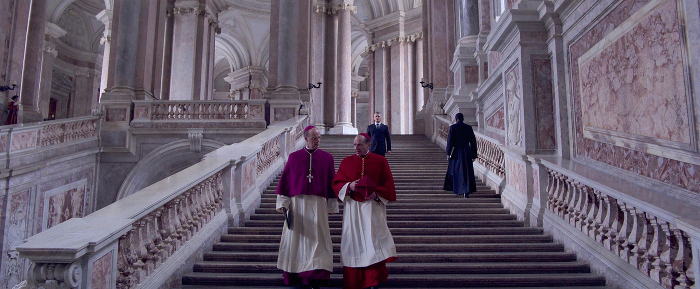 Imagine din filmul Conclave, cu doi dintre actori pe treptele unui clădiri